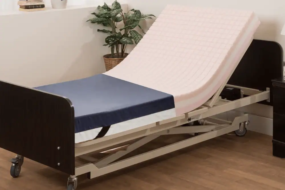 An adjustable hospital bed, classified as Durable Medical Equipment, with a foam mattress partially elevated, sits on wheels in a room featuring a potted plant and wooden flooring.