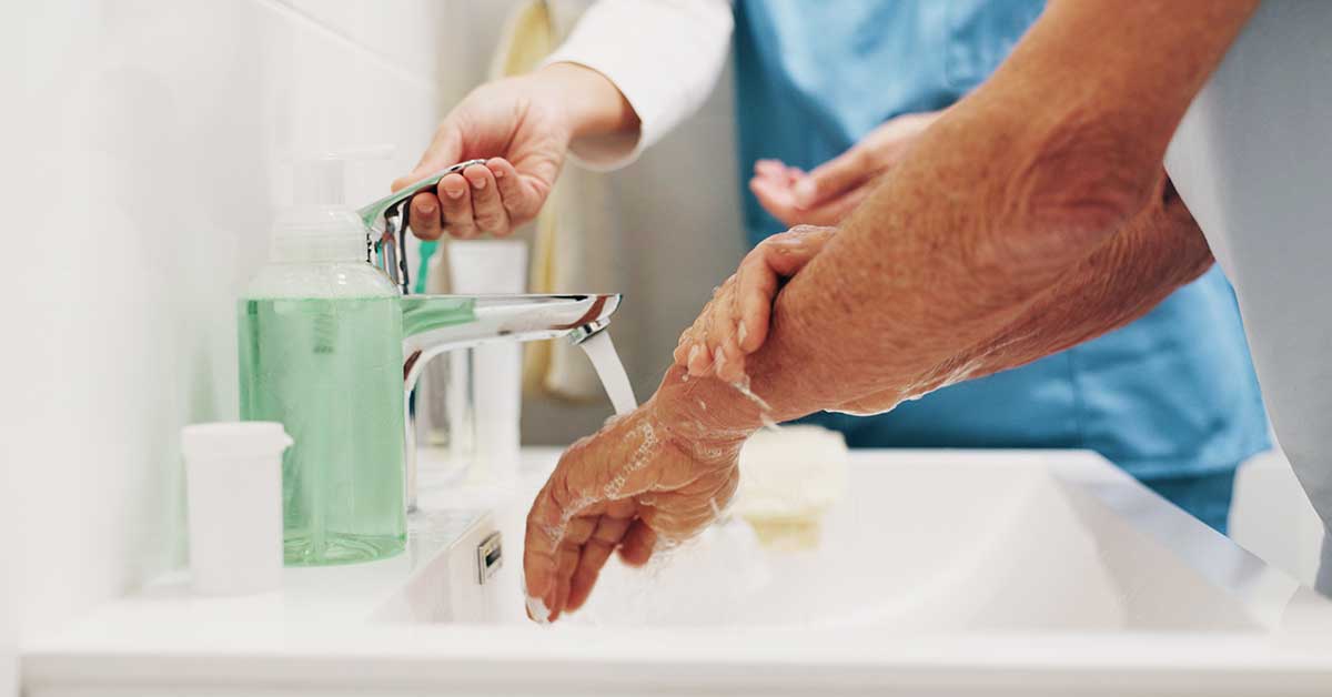 Two people washing their hands under running water at a sink, with soap and a dispenser visible on the counter—a crucial step in infection prevention during catheter care and for preventing UTIs.