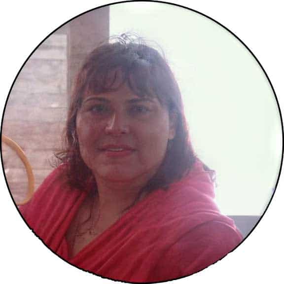 Kristin Hoffman, a woman with medium-length brown hair, wearing a pink top, sits indoors in front of a bright window.