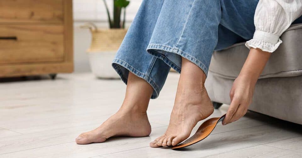 A person sitting on a couch places an orthopedic insole under their right foot, demonstrating proper Diabetes Foot Care.