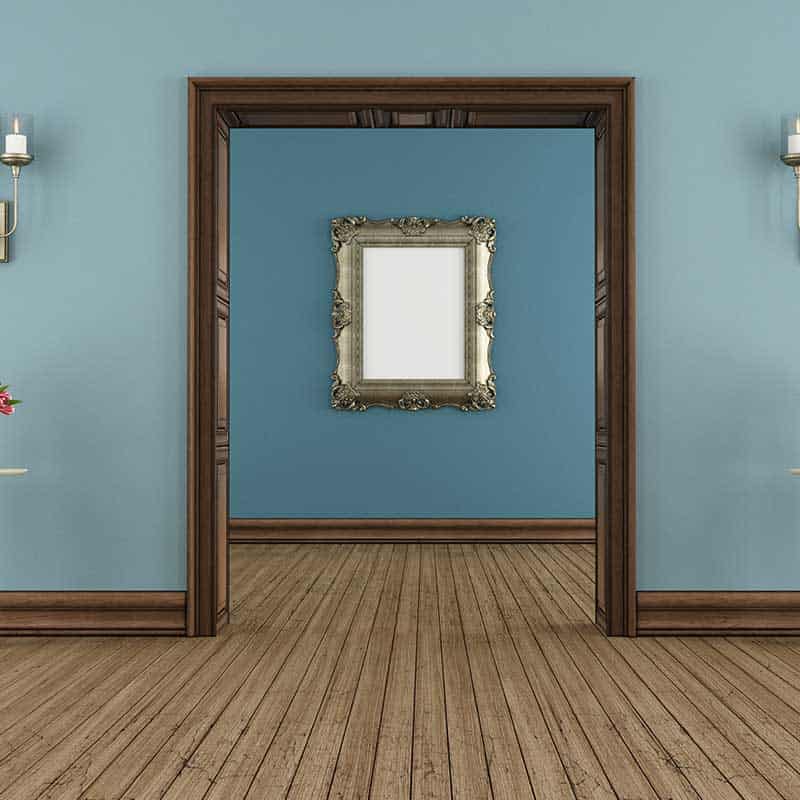 A wooden doorway frames a view of a blue-walled room with a decorative mirror on the back wall; hardwood floors and wall sconces are visible, showcasing the elegance possible with subtle Home Accessibility Solutions.