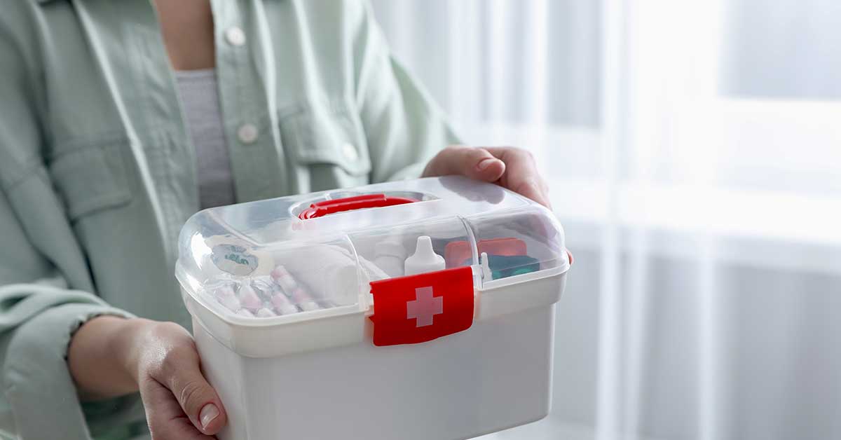 A person holding a white first aid kit with a red cross on the front, containing various medical supplies such as wound care dressings—a true caregiver’s guide for effective home healing, indoors.