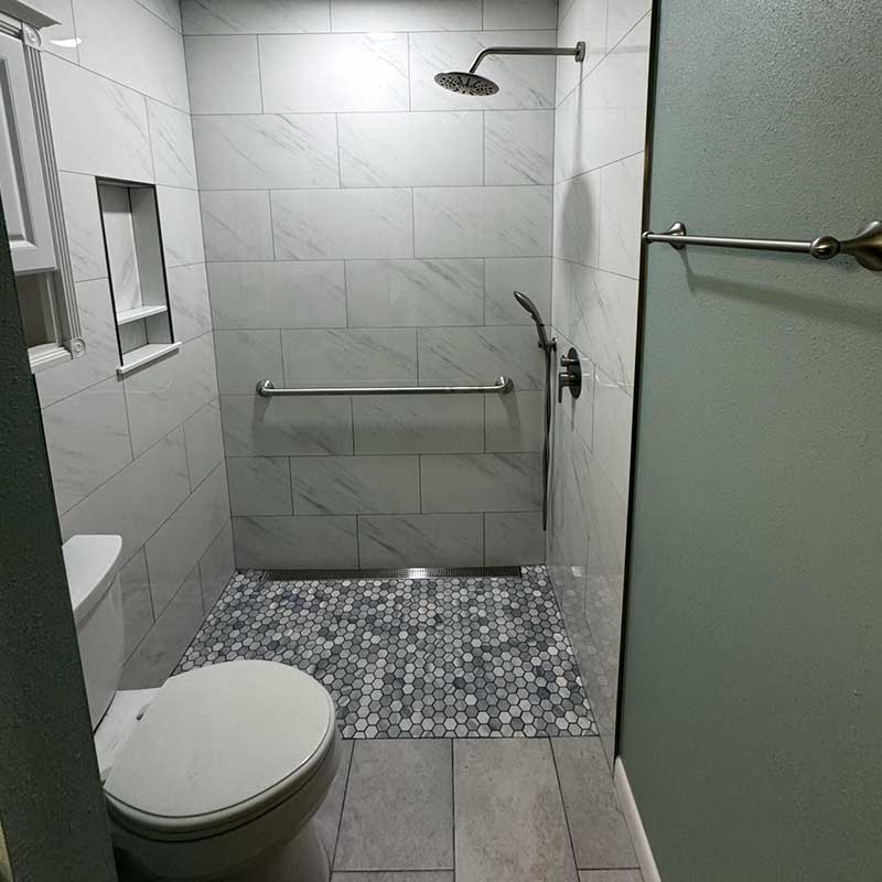 Accessible bathroom with walk-in shower, grab bar, handheld showerhead, hexagon tile floor in shower area, and toilet on the left—ideal for those needing Durable Medical Equipment.