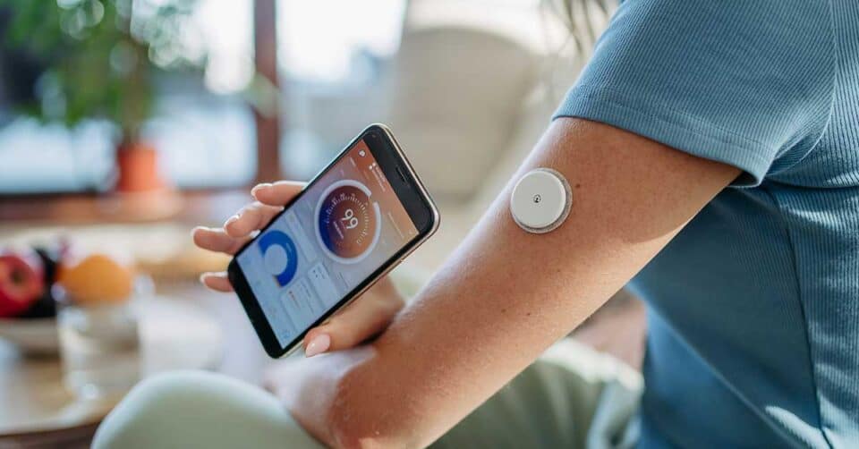Person using a smartphone to monitor glucose levels via a sensor attached to their upper arm, showcasing innovative wellness technology.