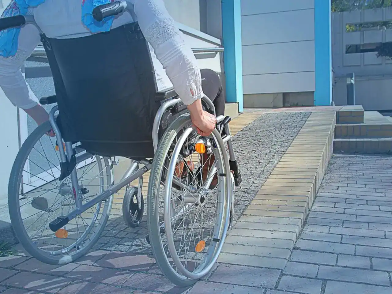 A person in a wheelchair moves up a wheelchair-accessible ramp next to a building, showcasing effective Home Accessibility Solutions.