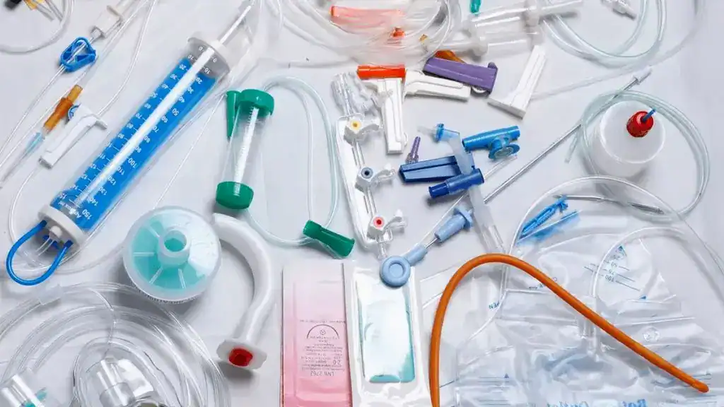 Various consumable medical supplies and disposable plastic equipment, including tubes, syringes, connectors, and bags, are spread out on a white surface.