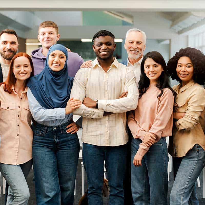 A diverse group of eight people stand closely together indoors, smiling at the camera.